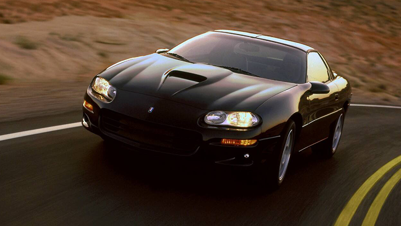 A black 1998 Camaro driving on a curve.