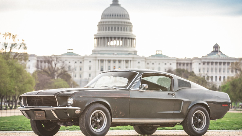 An army green Mustang sits in front of a government building.