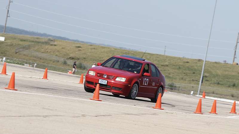 A red Volkswagen is on an autocross track marked by orange cones