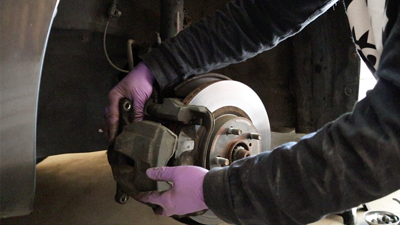 Two gloved hands are removing the caliper from the bracket.