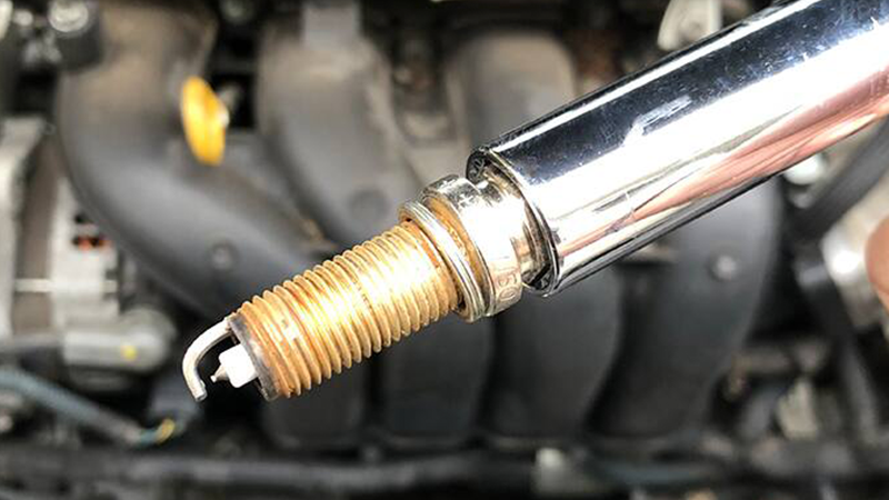 closeup of a spark plug in a socket with the engine in the background
