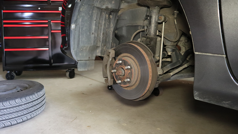 The left front view of a car with the wheel removed and placed on the floor. The brake rotor is visible. 