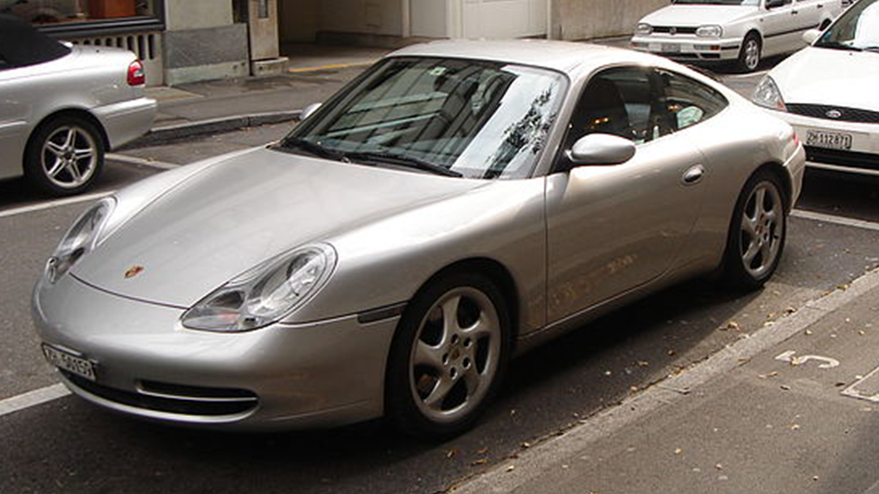 A silver Porsche parallel parked on the road.