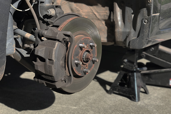 A car is jacked up on the left with the wheel removed, showing the brake rotor and caliper.