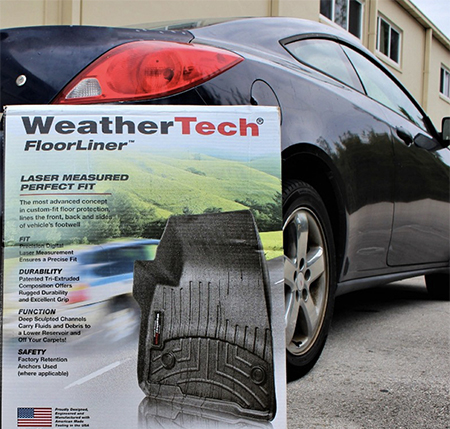 WeatherTech floor liner package displayed in front of a black 2008 Pontiac coupe