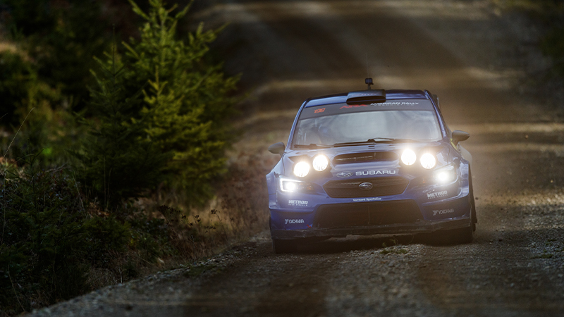 A rally car viewed from the front on a wooded track at night