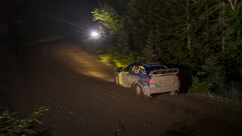 a view from the left rear of a rally car on a a dirt track at night