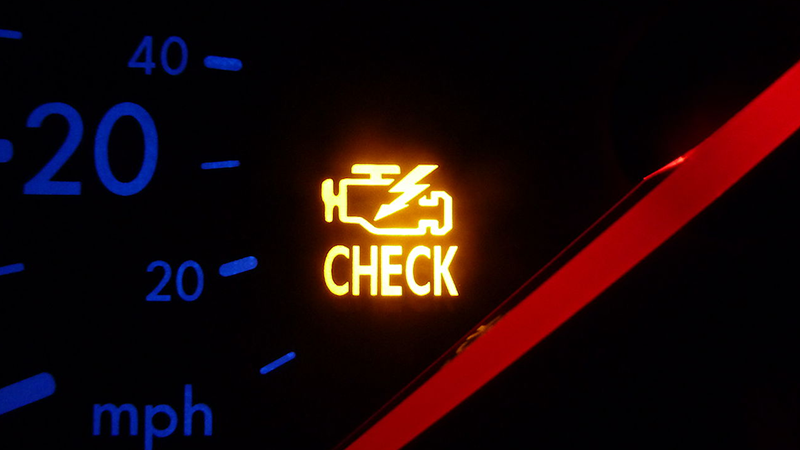 A yellow check engine light glows on a dark dashboard.