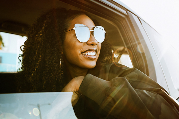 A young woman wearing sunglasses and a jacket looks out of an open car window