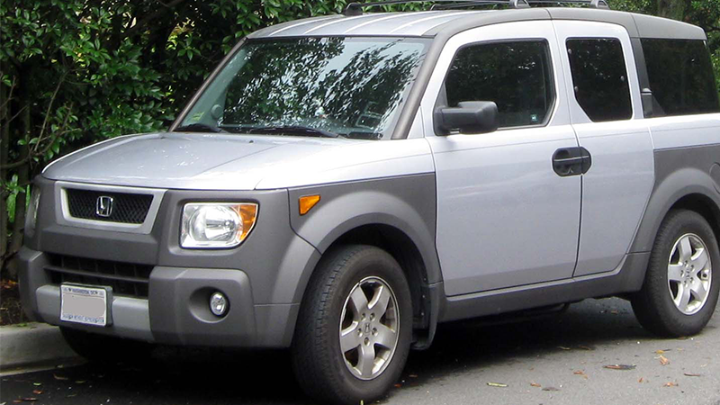 A silver and grey Honda Element parked next to a bush.