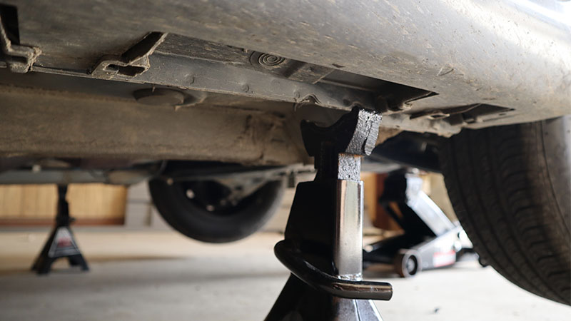 a jack stand positioned under the pinch weld of a vehicle raised by a floor jack