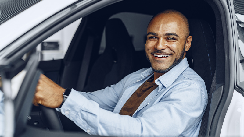 a smiling man sitting behind the wheel of a car
