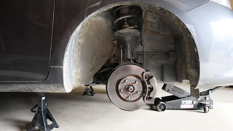 side view of a vehicle with the wheel removed, showing the disc brake and strut tower and coil spring