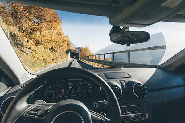 A view from the driver's seat of the steering wheel and view of a mountain landscape around the road ahead. Source | Riccardo Bresciani | Pexels