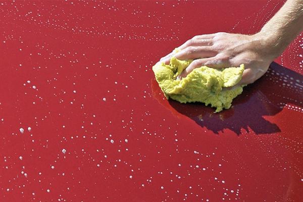a hand holding a yellow sponge washing a red car 