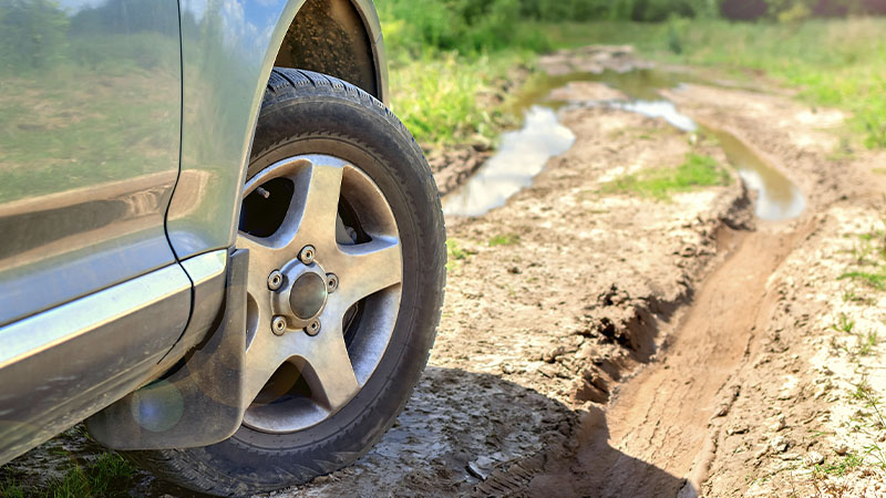 a side view of a car with a long, muddy road ahead