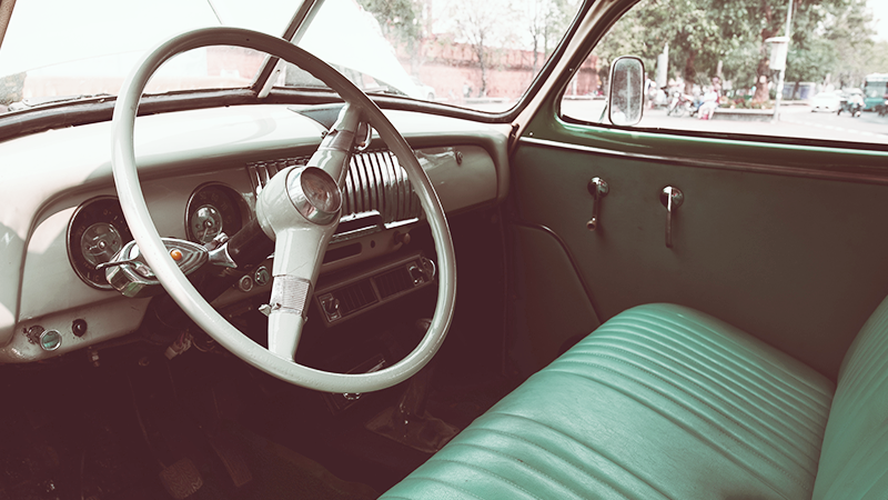 A view inside a vintage car with a large steering wheel and bench seat