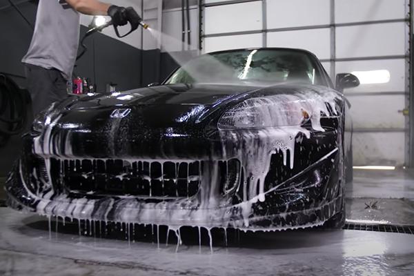 a black 1998 Honda S2000 CR is being sprayed with a foam canon by a professional detailer